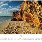 "Coral Bay", Kalender mit Sandstrand und felsigen Klippen, darüber blauer Himmel mit weißen Wolken.