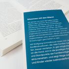 Ein blauer Umschlag mit weißem Text beschreibt die Herausforderungen und Lösungen für familiäre Konflikte und verbindet Eltern mit Kindern. Davor ein offenes Buch mit Fließtext.