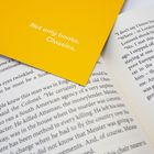 Text auf gelbem Papier: "Not only books. Classics." Liegt auf einem offenen Buch, dessen Textausschnitt teilweise sichtbar ist.