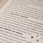Ein Ausschnitt aus einem Buch mit dem hervorgehobenen Text: "Seine Lippen näherten sich meinen." Daneben Herz- und Stern-Symbole.