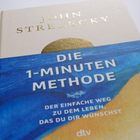 Auf einem Buchcover steht: "Die 1-Minuten Methode - Der einfache Weg zu dem Leben, das du dir wünschst". Unten ist ein Logo.