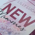 Text: "Lilly Lucas", "NEW Memories", "Roman". Pastelltöne, florales Motiv mit zarten Blüten im Hintergrund.