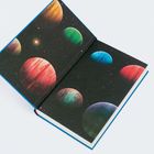Keine erkennbaren Texte. Ein geöffnetes Buch zeigt eine Illustration mit bunten Planeten und Sternen im Weltraum auf dunklem Hintergrund.