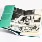 Ein Buch, offen mit einem grünen Umschlagtext. Schwarz-weiß Foto: Person schaut aus einem Autofenster.