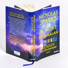 Ein Buch mit dem Titel "REMAIN - WAS VON UNS BLEIBT" von Nicholas Sparks und M. Night Shyamalan, blauer Himmel im Hintergrund.