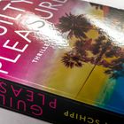 "GUILTY PLEASURE" in großen weißen Buchstaben. Darunter: "THRILLER". Hintergrund: Sonnenuntergang mit Palmen.