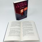 "Camilla Läckberg, Revenge, Die Rache einer Frau ist schön und brutal." Ein Taschenbuch und ein aufgeschlagenes Buch.
