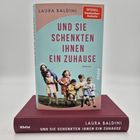 "Und sie schenkten ihnen ein Zuhause" von Laura Baldini. Cover zeigt fröhliche Kinder auf einer Wiese. Buch liegt auf rotem Band.