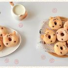 Illustration einer Katze mit Donut. Donuts auf Tellern, geformt wie Katzenköpfe mit Schokoladendekor. Kanne mit Milch.