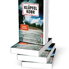 "KLÜPFEL KOBR Laienpiel Kriminalroman" auf Buchcover, daneben liegt ein geöffnetes Buch.