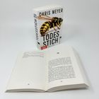 "CHRIS MEYER TODESSTICH" steht groß auf einem Buch mit einer Wespe. Daneben liegt das geöffnete Buch auf Seite 162/163.