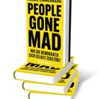 Das Bild zeigt ein gelbes Buchcover mit dem Titel "People Gone Mad: Wie die Demokratie sich selbst zerstört" von Moshe Zimmermann. Davor liegt das Buch geöffnet aufgeschlagen auf Seite 182 und 183.