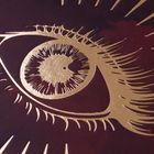 Ein kunstvoll gezeichnetes Auge in Gold auf dunklem Hintergrund, mit strahlenförmigen Linien ringsum.