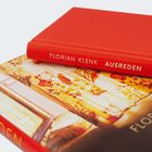 "FLORIAN KLENK AUSREDEN" steht auf einem roten Buchrücken. Darauf liegt ein blumiges Buchcover.