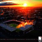 05 2027, Mai Kalender; Fußballstadion bei Sonnenuntergang, Stadt im Hintergrund, Stadionlichter und Rauch sichtbar.