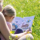 Ein Kind liest mit einem Erwachsenen in einem blühenden Feld ein Buch über Tiere.