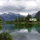 ALMTAL. Ein klarer See reflektiert Bäume und Berge unter einem bewölkten Himmel. üppige Vegetation im Vordergrund.