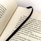 Ein aufgeschlagenes Buch mit Textpassagen und einem schwarzen Stoffband als Lesezeichen.