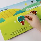 "Auf der Wiese" und "Welche Tiere leben auf der Wiese? Klebe eine Kuh, ein Pferd und ein Schwein ein. Wer von ihnen wälzt sich im Schlamm?" Ein Kinderbuch mit Tieren und Hand, die einen Baum platziert.