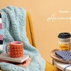 „Season 4: Accessoires“; gestrickte Decke, bunte Streifenschals, Tasse, Bücher, Becher mit Hülle, Sonnenbrille, Klammer.