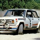 Auf einem staubigen Weg fährt ein Rallyeauto mit der Startnummer 5. Es trägt Werbung von "Hella" und "Mobil".