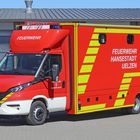 "FEUERWEHR HANSESTADT UELZEN," rotes Feuerwehrfahrzeug mit gelben Streifen, IVECO-Logo, vor einer Halle.
