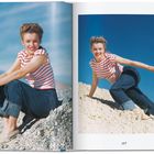 Nummer 107. Eine Frau in rot-weiß gestreiftem Shirt und Jeans sitzt und kniet lächelnd auf steinigem Untergrund.