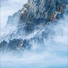 Mai-Kalenderbild mit felsiger Landschaft und Ziegen. Im Hintergrund Nebelschwaden und blauer Himmel.