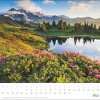 Kalender für Mai; bunte Alpenlandschaft mit Blumen, Bäumen und einem See, im Hintergrund Berge mit Schnee.