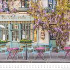 "Au Vieux Paris" auf einem grünen Schild, umrankt von lila Blüten. Davor bunte Tische und Stühle, Monat Mai unten.