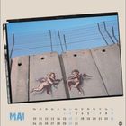 „MAI“ und Kalenderdaten unten. Illustration: Zwei Putten an Betonmauer mit Stacheldraht.