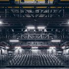 Ein leerer Theatersaal mit schwarzen Sitzreihen, Bühnentechnik und Beleuchtung an der Decke.