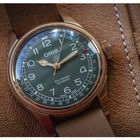 Text: ORIS, BIG CROWN AUTOMATIC. Eine Armbanduhr mit braunem Lederarmband auf einer genarbten Lederoberfläche.