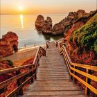 Kalender: Monat Mai 2027. Eine Holztreppe führt zu einem Strand bei Sonnenuntergang, flankiert von Felsen und Meer.