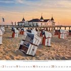 5/2023, Monatskalender. Strandkörbe auf Sand vor einer Seebrücke mit einem großen Gebäude. Der Himmel ist orange gefärbt.