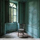 Text: "5 2027, 1 2 3 [...] 29 30 31." Ein leerer, verfallener Raum mit bläulich-grünen Wänden und einem einfachen Holzstuhl.