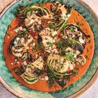 Gerösteter Blumenkohl auf roter Sauce, garniert mit Kräutern und Nüssen, serviert auf einem grünen Teller.