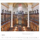 Text: "Literatur muss nicht nur Fragen beantworten, sie muss auch Fragen aufwerfen." - Doris Niespos. 

Beschreibung: Eine historische Bibliothek mit hohen Decken, Säulen und Bücherregalen.