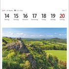"Woche 24, 14-20 Juni. Bild: Felsen und grüne Felder unter blauem Himmel im Naturpark Hessische Rhön."