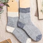 Keine Texte sichtbar. Zwei gestrickte Socken auf Holzformen, daneben Pflanzen und Notizheft auf gestricktem Untergrund.