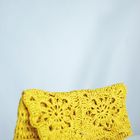 Kein Text sichtbar. Eine gelbe, gehäkelte Tasche mit Blumenmotiv auf grauem Hintergrund.