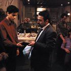 Ein Mann in einem Anzug übergibt einem jungen Mann ein Objekt, während mehrere Personen in einem Restaurant interagieren.