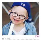 "Junge mit Eis", Kalender Mai. Ein fröhliches Kind mit Brille und Cap, hält Eis und lächelt.