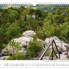 Kalenderseite Mai, zeigt ein Waldgebiet mit Treppen und Felsen auf einem Hügel, umgeben von üppigem Grün.