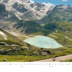 Kalenderseite mit dem Monat "Mai". Ein Radfahrer auf einer Bergstraße, im Hintergrund ein See und schneebedeckte Berge.