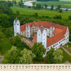 Monatsnamen und Zahlen in Kalenderformat. Zinnen-Schloss mit rotem Dach, umgeben von Bäumen und Wiesen, im Hintergrund ein Fluss.