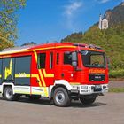 "Feuerwehr Schwangau" steht auf einem roten Feuerwehrauto vor einem Wald. Berg und Schloss im Hintergrund.