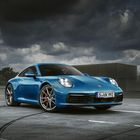 Nummernschild: "S VK 992". Ein blauer Sportwagen steht auf einem Parkplatz unter einem dramatisch bewölkten Himmel.
