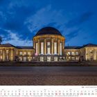 "DB KÖLN MESSE/DEUTZ" steht in der Mitte. Majestätisches Gebäude bei Dämmerung, Frontansicht, mit Uhr oben und Bäumen.