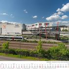 Remscheid Hauptbahnhof mit Else-Treichel-Steg. Ein moderner Zug auf Gleisen, weiße Gebäude, blauer Himmel mit Wolken. Mai 2027 Kalender.
